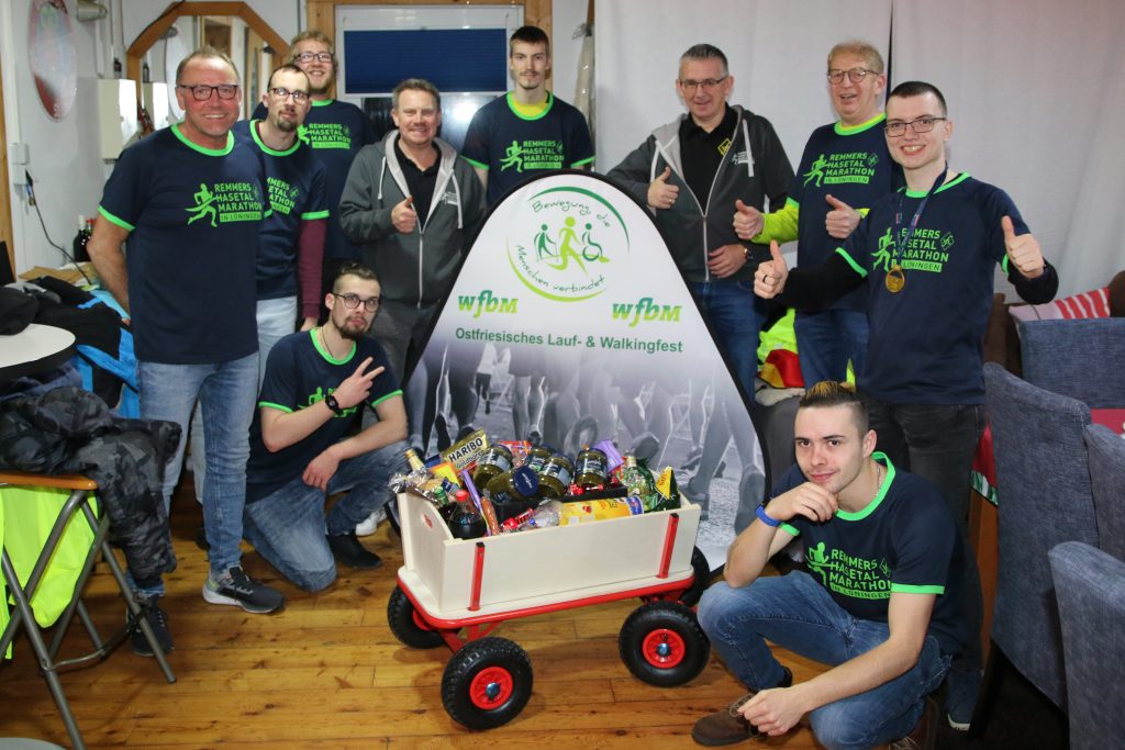 zum Bild;Das Kollegium der Werkstätten für behinderte Menschen (wfbm) Aurich-Wittmund freute sich sehr bei der Übergabe des gewonnenen Preises als „kreativstes Team“. Der Preis wurde übergeben von Jens Lüken und Stefan Beumker (Bildmitte) vom Löninger Marathon-Organisationsteam. Wfbm-Laufchef Hermann Rößing (links im Bild) strahlt mit einem Teil der beteiligten Athleten um die Wette. Foto: Remmers-Hasetal-Marathon. Hinweis zum Foto: Alle auf dem Foto sind gegen Corona geimpft und wurden vor der Aufnahme negativ auf Corona getestet, daher entfiel die Maskenpflicht.